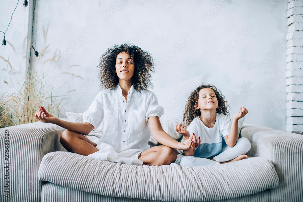 woman and child sitting on couch with eyes closed and arms extended outward and hands facing upward as they try meditating